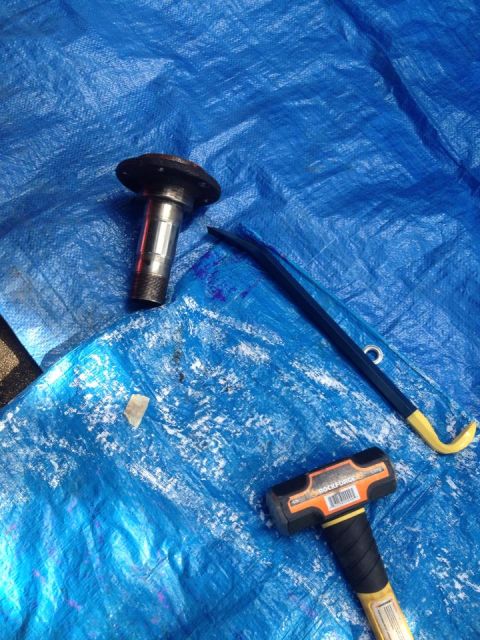 1990 Ford Bronco - An automotive part, a pry bar, and a sledgehammer are laid out on a blue tarp, suggesting a repair or disassembly process.