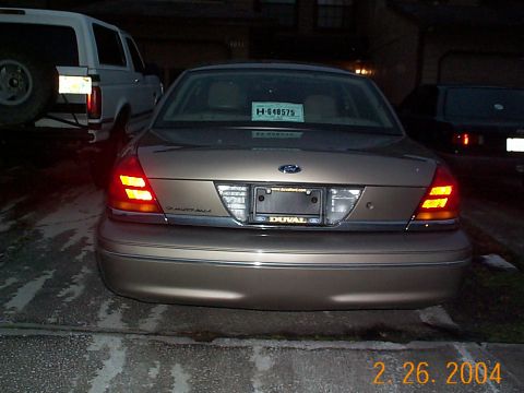 2003 Ford Crown Victoria - A tan sedan is parked in a driveway at night, with a white SUV and another dark vehicle also visible.
