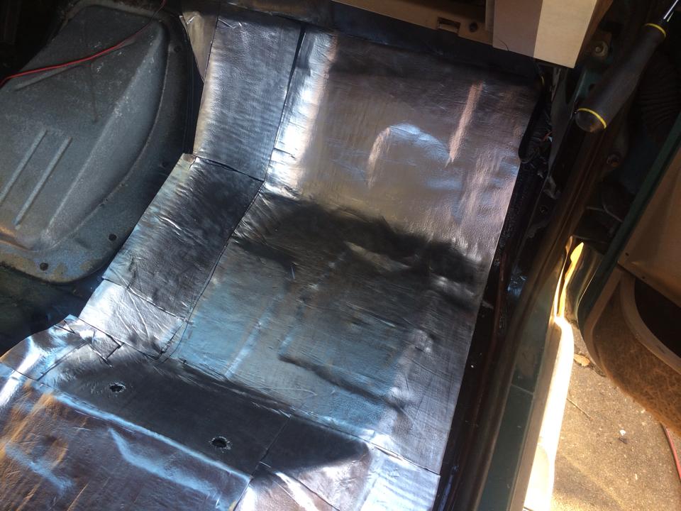 Vehicle floor covered in silver insulation material, showing part of the wheel well