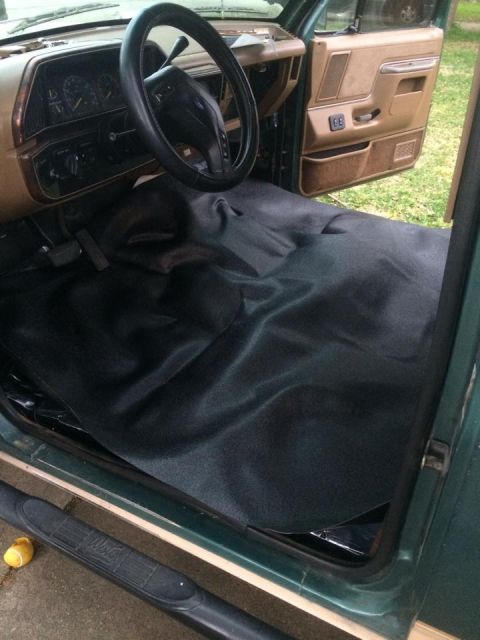 1990 Ford Bronco - The interior of a 1990 Ford Bronco shows a black floor liner and tan door panel.