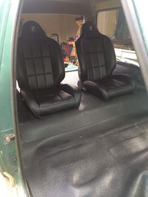 1990 Ford Bronco - The interior of a green vehicle shows newly installed black bucket seats and a black floor mat.
