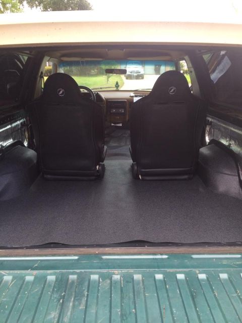 1990 Ford Bronco - The interior of a vehicle shows two black seats and a gray carpeted floor, with a dashboard visible ahead.