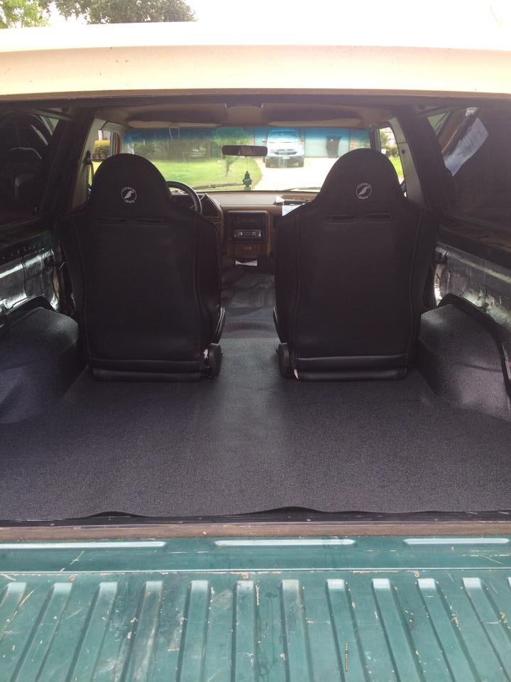 Vehicle interior with two black seats, gray carpeted floor, and dashboard visible. A "SUPERMOTORS" watermark is present