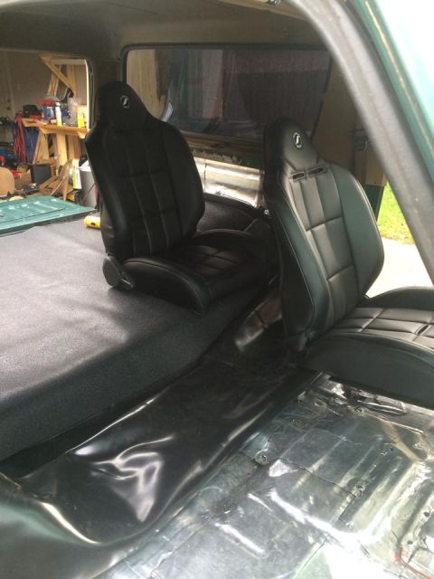 1990 Ford Bronco - The interior of a vehicle shows black bucket seats and a partially finished floor with exposed metal.