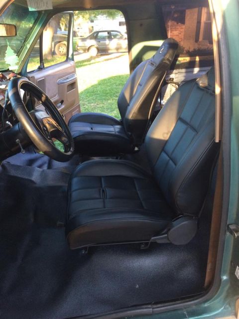 1990 Ford Bronco - Front cab of a truck showing black vinyl bucket seats, a wrapped steering wheel and dark carpeting.