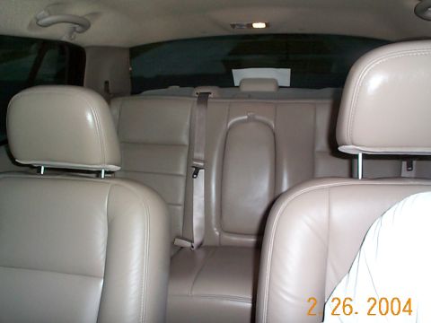 2003 Ford Crown Victoria - Interior view of tan leather rear car seats and headrests, showing a seatbelt and the car's interior lighting.