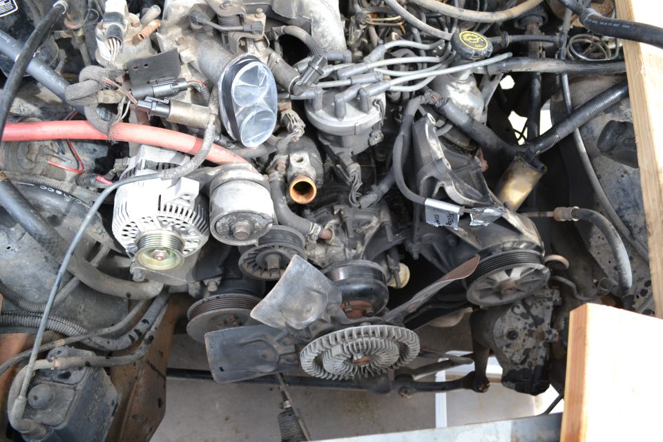 Engine bay with alternator, distributor, fan, and hoses visible. Some text on a sticker is readable