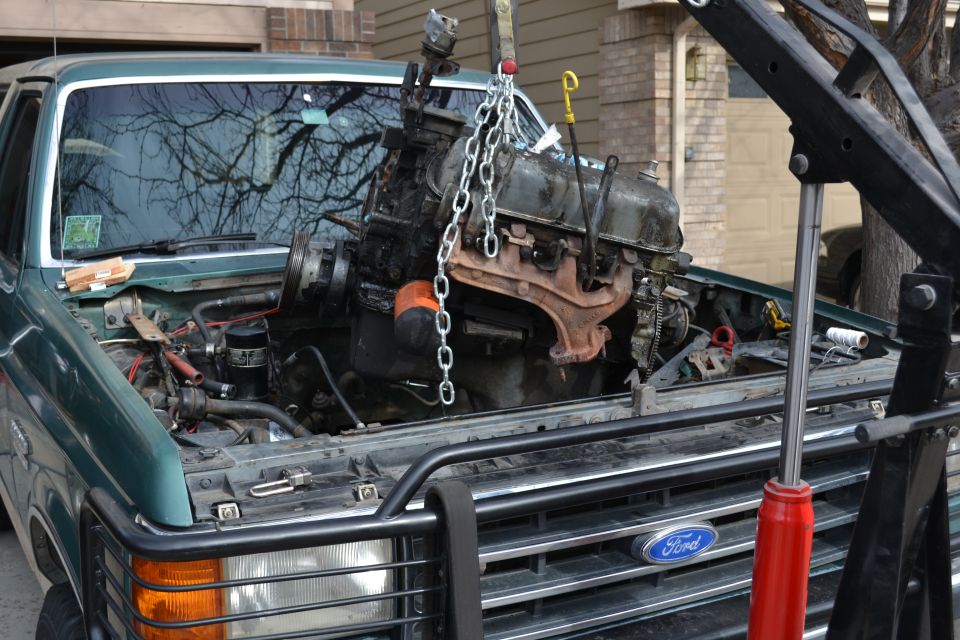 Green 1990 Ford Bronco with engine being removed by a crane