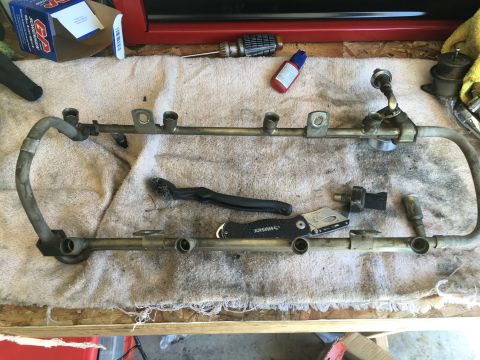 1987 Ford Bronco - A disassembled fuel rail assembly is laid out with various tools for maintenance or repair.