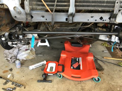 1987 Ford Bronco - The underside of a vehicle is shown with various mechanical parts and a mechanic's creeper on the ground.