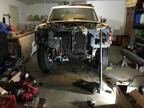 1987 Ford Bronco - A 1987 Ford Bronco is shown in a garage with its front end disassembled, likely undergoing repairs or a rebuild.