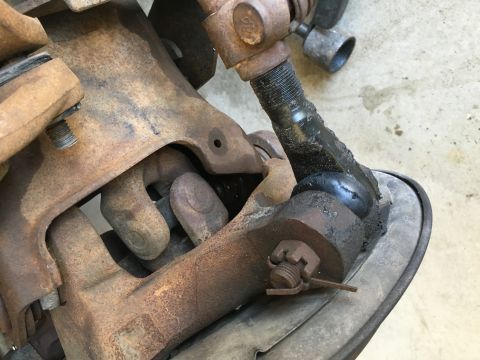 1987 Ford Bronco - Close-up view of a heavily rusted suspension component, likely a ball joint and tie rod end assembly.