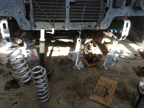 1987 Ford Bronco - Front end of a vehicle undergoing suspension work, with parts laid out on the garage floor.