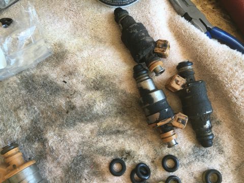 1987 Ford Bronco - Four dirty fuel injectors and O-rings are laid out on a towel, possibly for a rebuild or replacement.