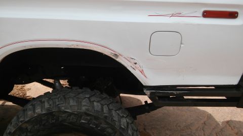 1979 Ford Bronco - The side of a white 1979 Ford Bronco shows damage and red pinstripes near the rear wheel well.