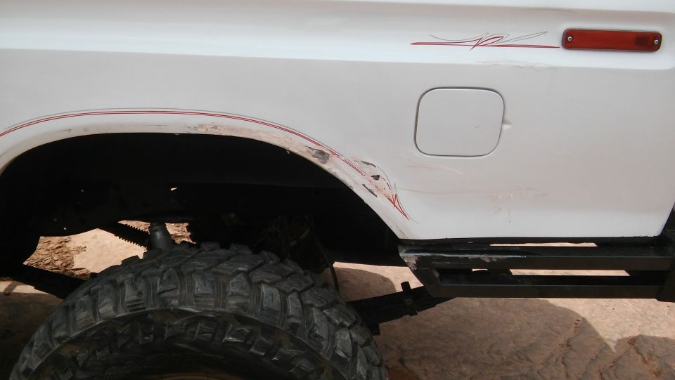 White 1979 Ford Bronco side view with red pinstripes and damage near the rear wheel well