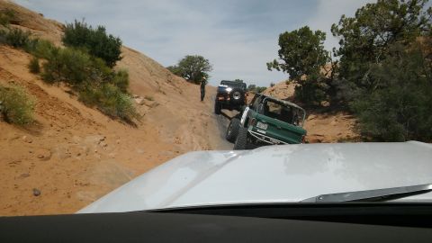 1979 Ford Bronco - Multiple off-road vehicles navigate a steep, rocky incline under a partly cloudy sky.