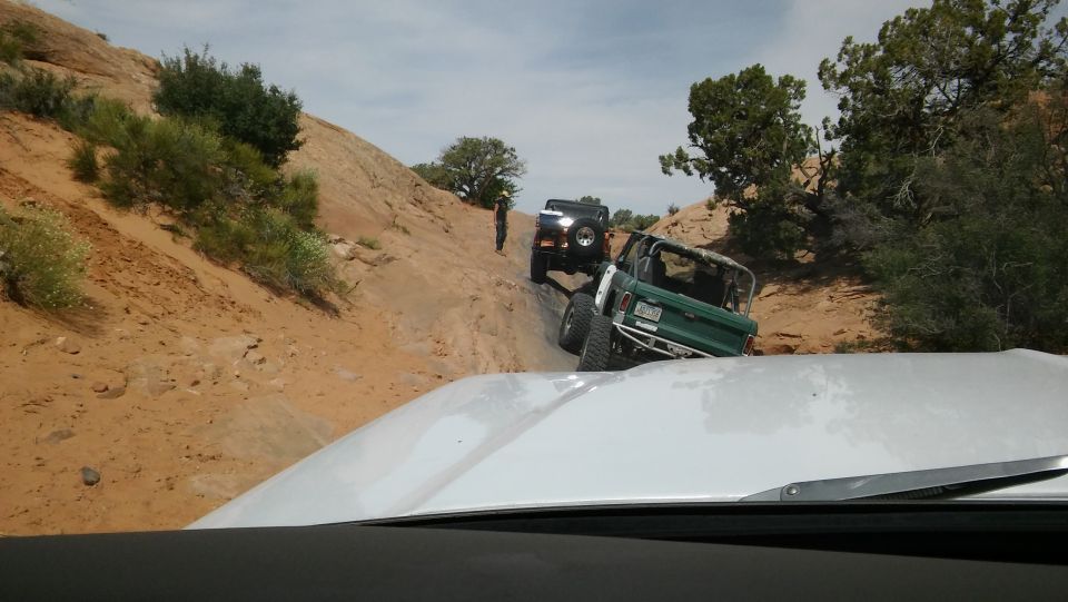 Green SUV with roll cage on rocky trail, rear view. Modified body, aftermarket bumper
