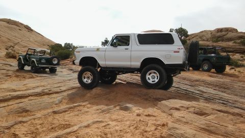 1979 Ford Bronco - A lifted white 1979 Ford Bronco is parked on a rocky trail with two other off-road vehicles in the background.