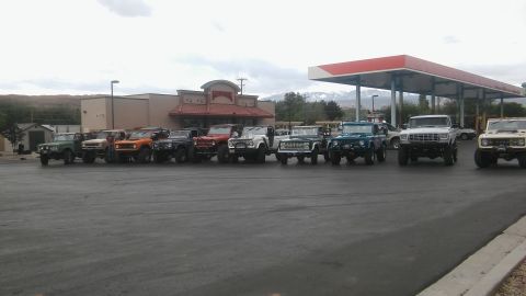 1979 Ford Bronco - A group of Ford Broncos and other SUVs are lined up in a parking lot near a gas station.