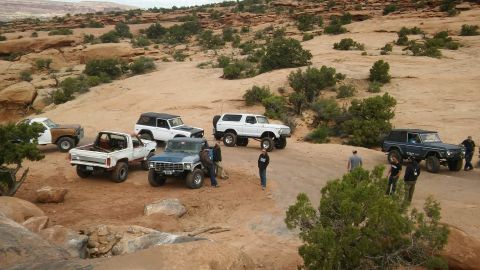 1979 Ford Bronco - A group of off-road vehicles are gathered on a dusty trail surrounded by desert terrain and sparse vegetation.