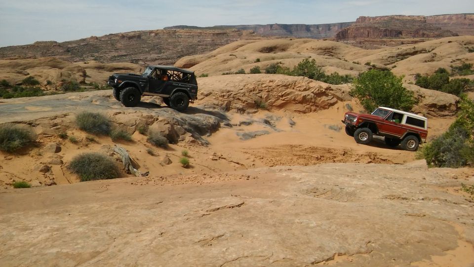 Two Ford Broncos, one black and one red with white top, navigate rocky desert terrain