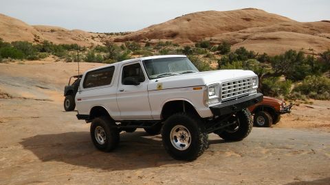 1979 Ford Bronco - Two off-road vehicles, a white Ford Bronco and an orange Toyota Land Cruiser, are parked in a desert landscape.