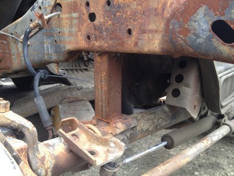 1979 Ford Bronco - Close-up view of a heavily rusted vehicle chassis frame, showing brake lines and suspension parts.
