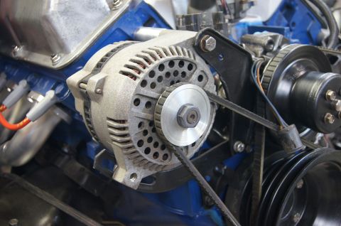 1979 Ford Bronco - Close-up view of an alternator and associated engine components, including belts and pulleys, mounted on a blue engine block.