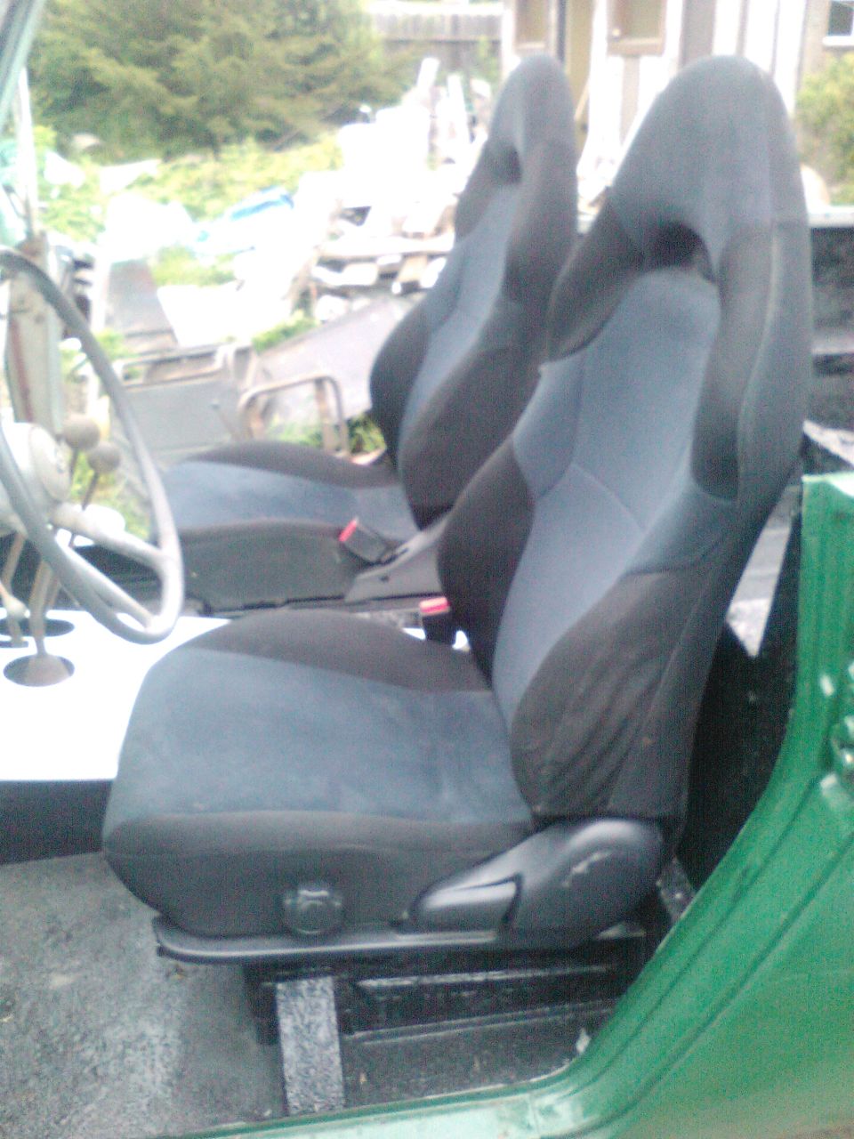 Two bucket seats inside a green vehicle, with a steering wheel visible on the left