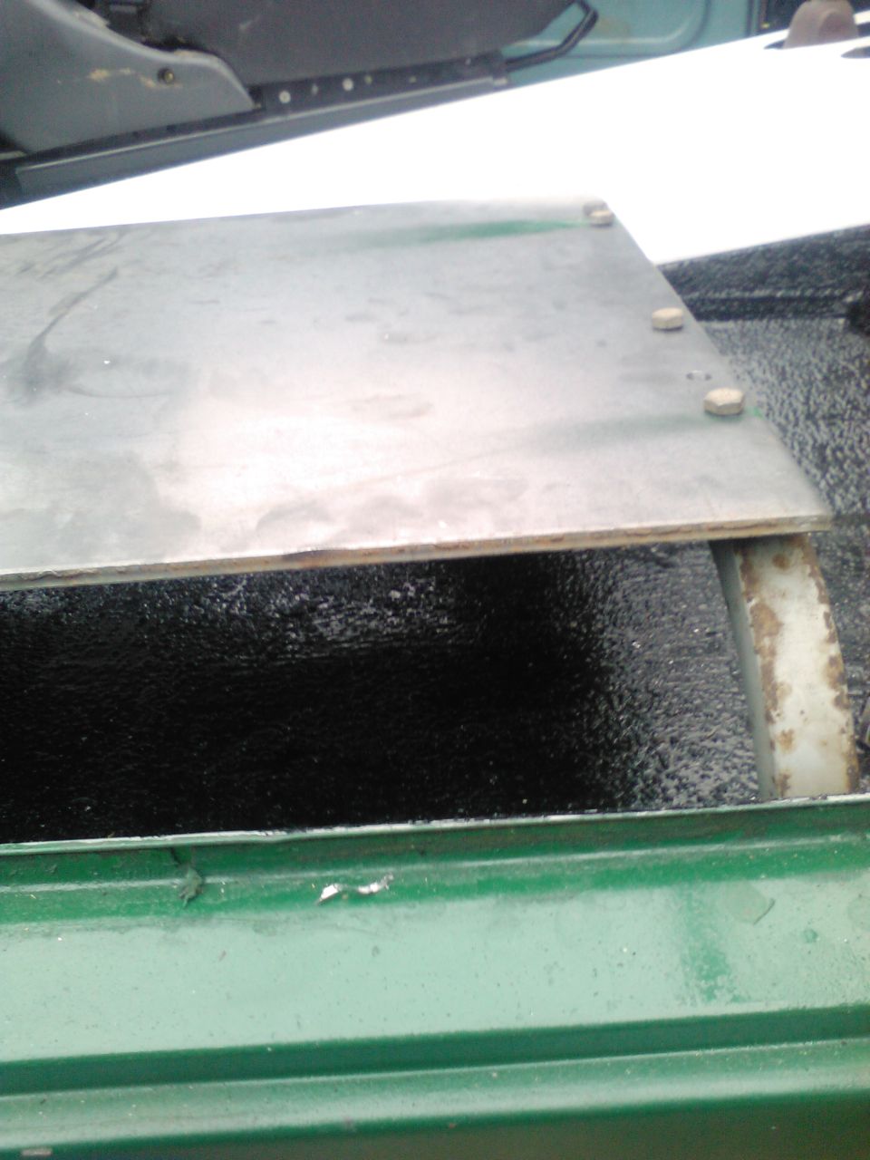 metal plate bolted down in green truck bed, part of seat visible above