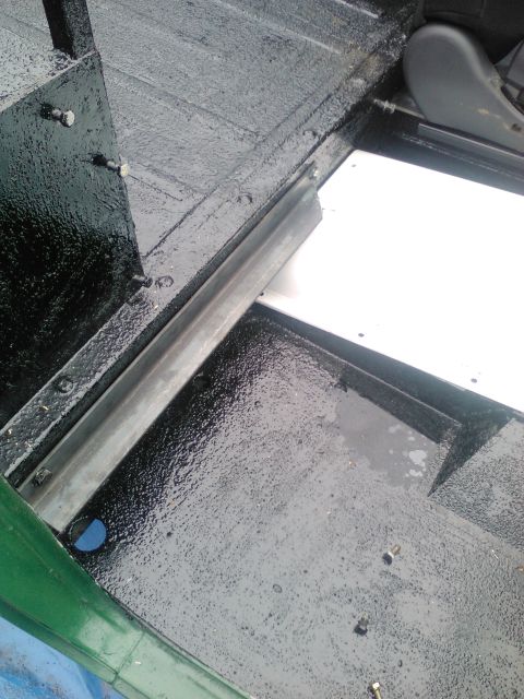 1991 Ford Bronco - The interior floor of a vehicle shows a black textured coating and a metal rail, with a white panel in view.