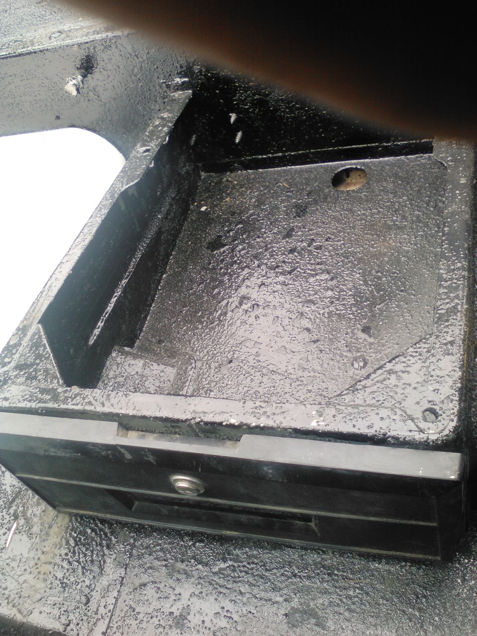 Black metal compartment with a silver latch, showing textured surface and some wear