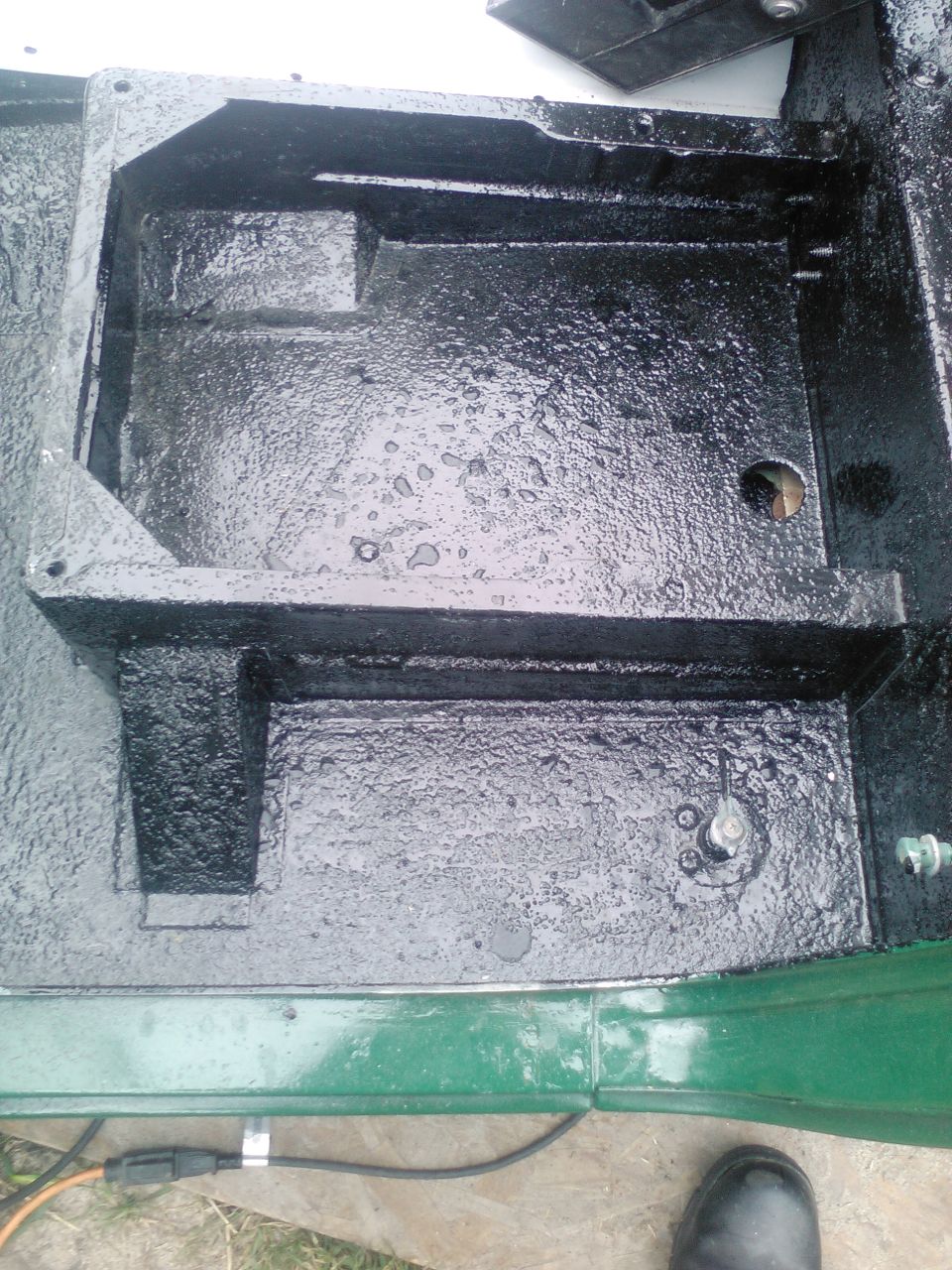 Black painted metal chassis component with visible bolts and a circular opening