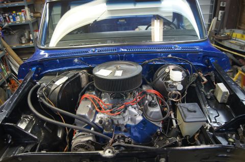 1979 Ford Bronco - The engine bay of a blue pickup truck is shown with its V8 engine and various components.
