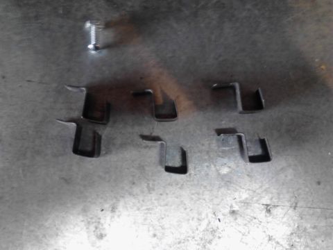 1990 Ford Bronco - Several metal clips and a single screw are laid out on a metallic surface, possibly for a repair or project.