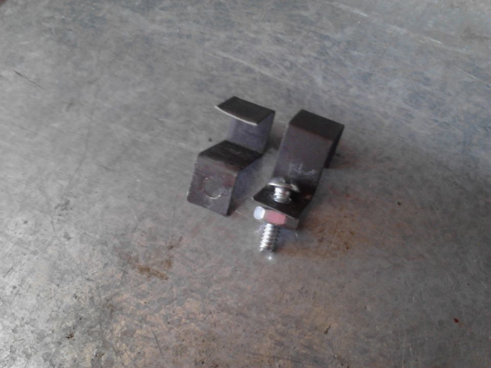 Two metal brackets, one with a bolt and washer attached, on a textured metal surface
