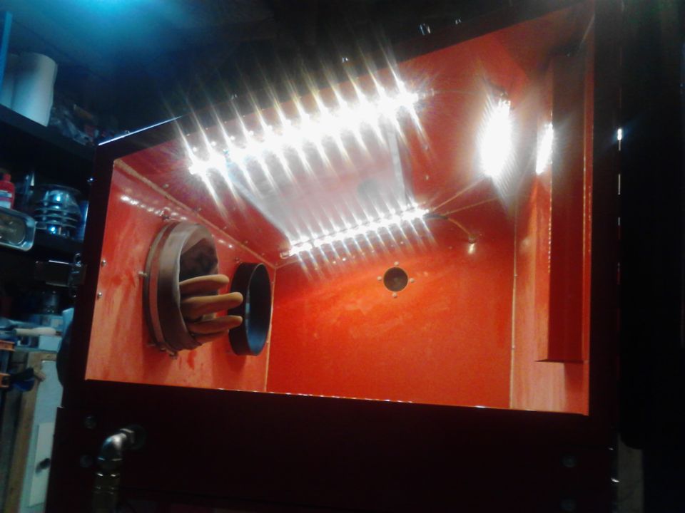 Interior of a red sandblaster cabinet with lights and glove ports