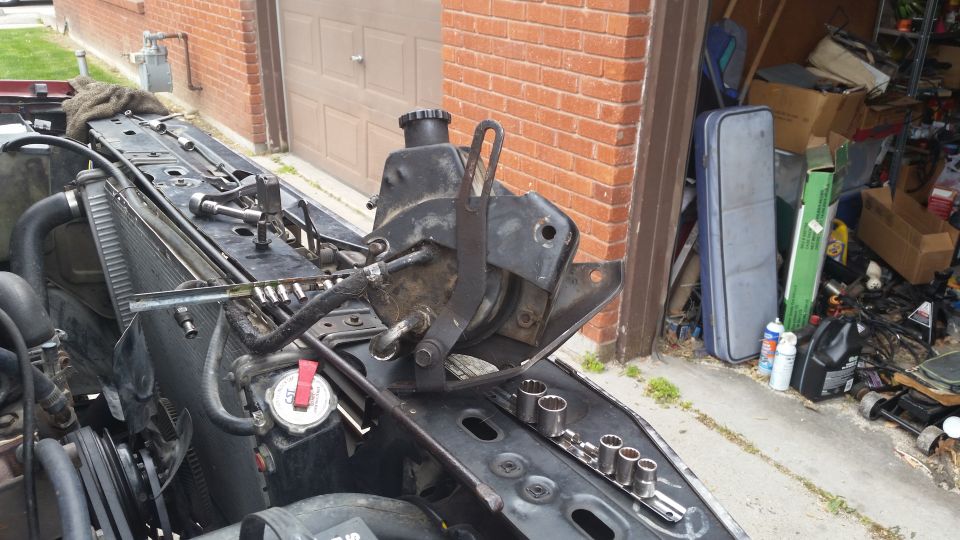 Power steering pump assembly removed from vehicle, resting on engine bay components