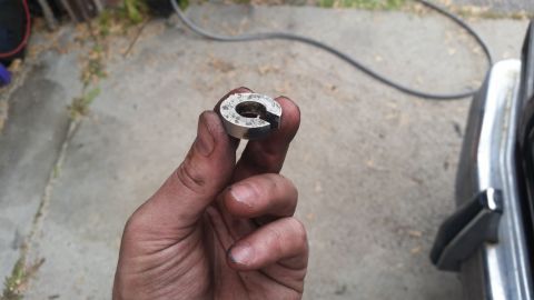 1981 Ford Bronco - A metal spacer part is held in a dirty hand, with a portion of a vehicle visible in the background.