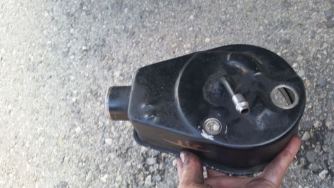 1981 Ford Bronco - A black power steering pump is held by a hand against a gravelly surface, with a Supermotors.net watermark visible.