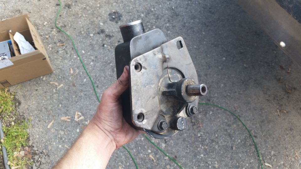 Hand holding a power steering pump with mounting bracket