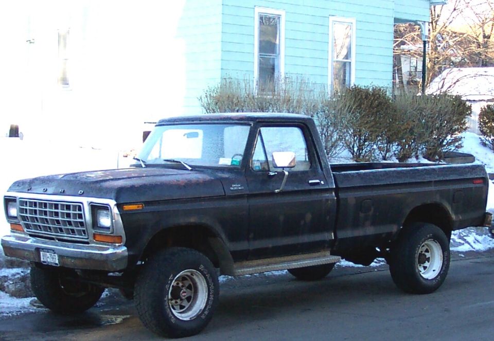 Side view of a faded 1970s Ford pickup parked by a blue house in winter