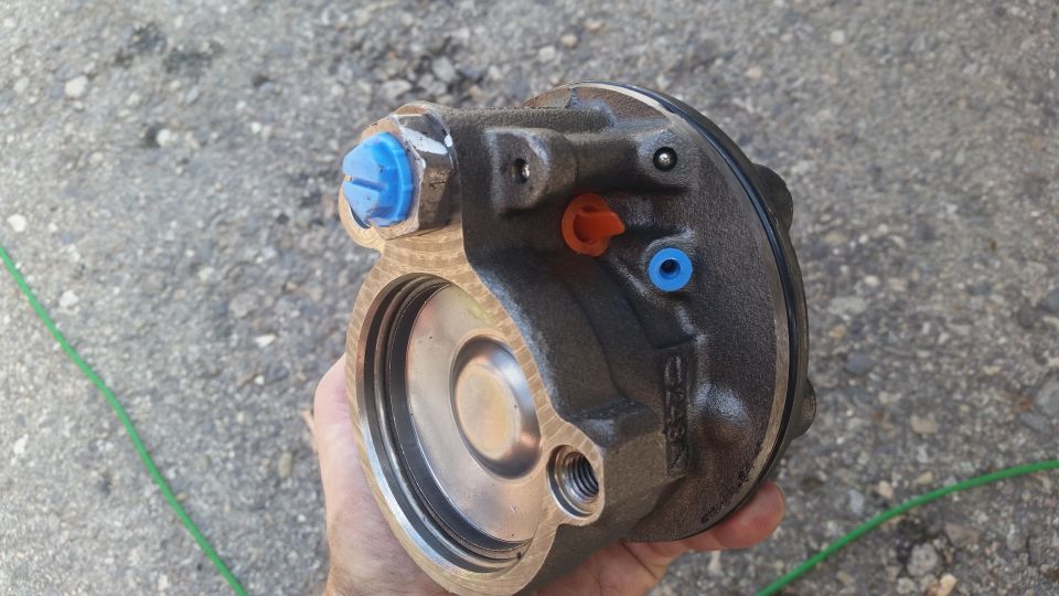 Hand holding a power steering pump with blue and orange caps on fittings