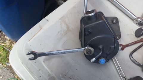 1981 Ford Bronco - A power steering pump is shown with a wrench attached, resting on a white surface next to other tools.