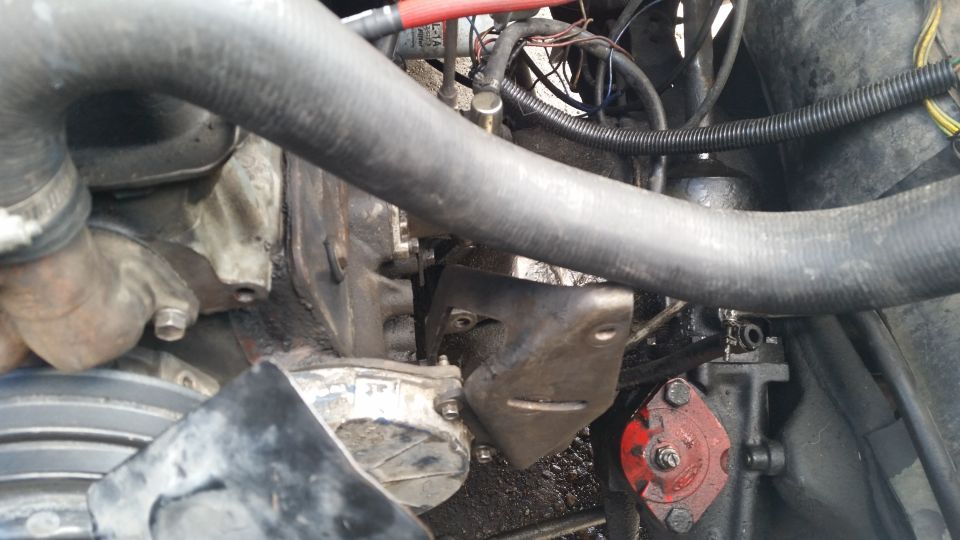 Close-up of engine bay with hoses, wires, and metal brackets visible. A red component with 'SUPERMOTORS' logo is in the lower right