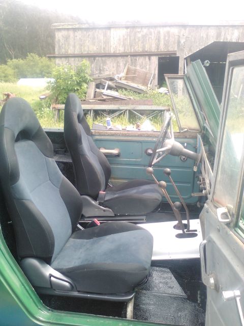1991 Ford Bronco - The interior of a green off-road vehicle shows two aftermarket bucket seats and a manual transmission shifter setup.