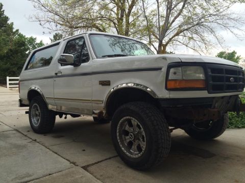 1995 Ford Bronco - A white Ford Bronco is parked on a concrete driveway with trees in the background.