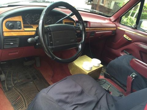 1995 Ford Bronco - The interior of a 1995 Ford Bronco features wood grain accents on the dashboard and door panels, complemented by red upholstery.