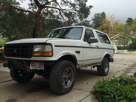 1995 Ford Bronco - This 1995 Ford Bronco is shown from a three-quarter front view, parked on a paved surface with residential buildings and foliage visible.